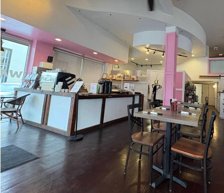 The bright cafe interior with pink pillars, the counter and wooden tables